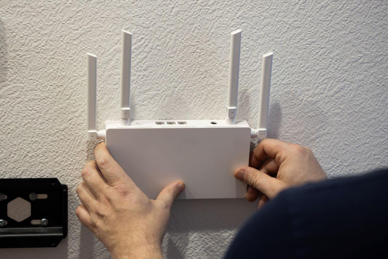 Haende montieren Router mit Antennen an weisse Wand – praktische Anwendung von FTTH Zubehoer im privaten Netzwerk