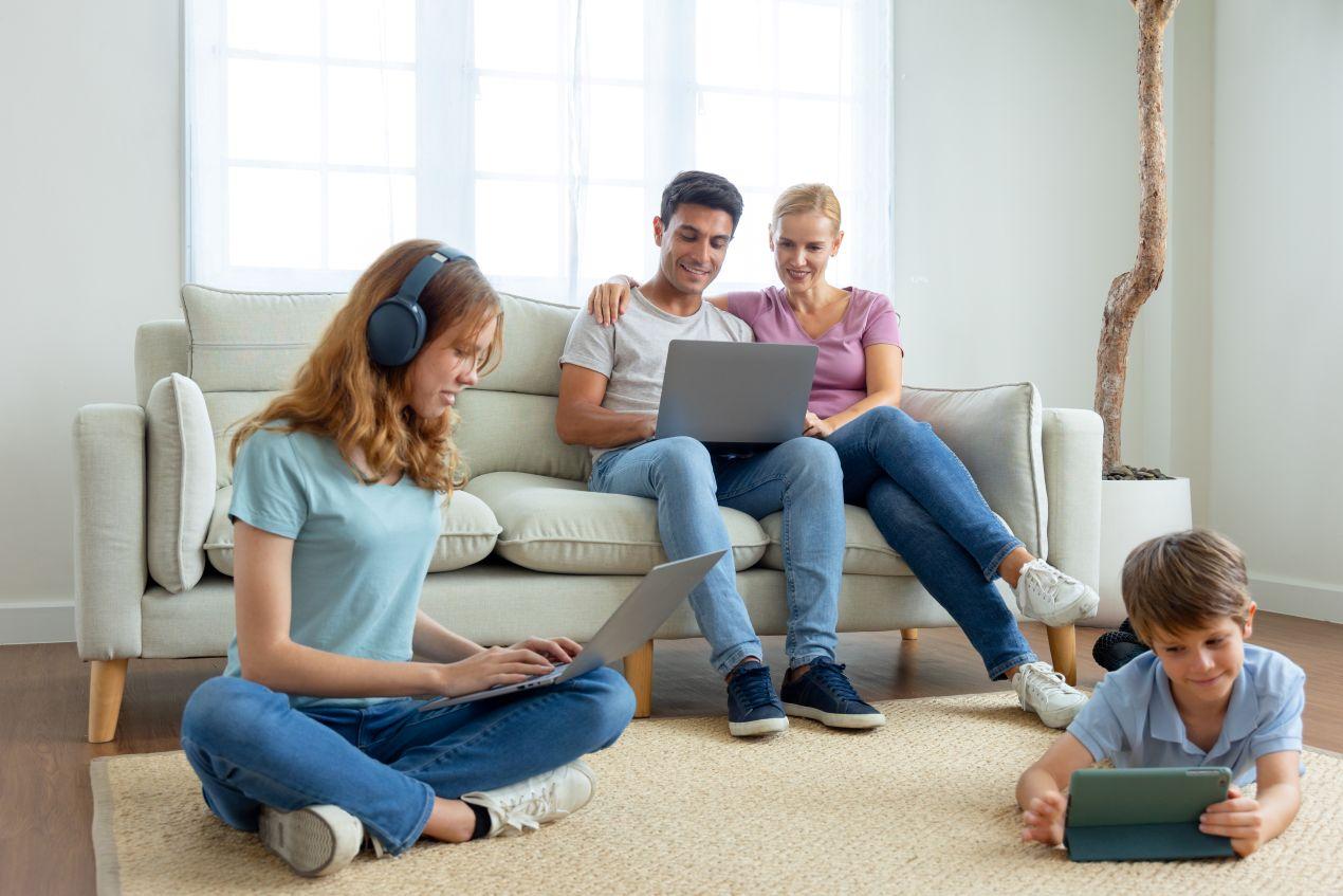 Familie nutzt Laptop, Tablet und Kopfhörer im Wohnzimmer – stabiles Internet durch hochwertiges FTTH Zubehoer